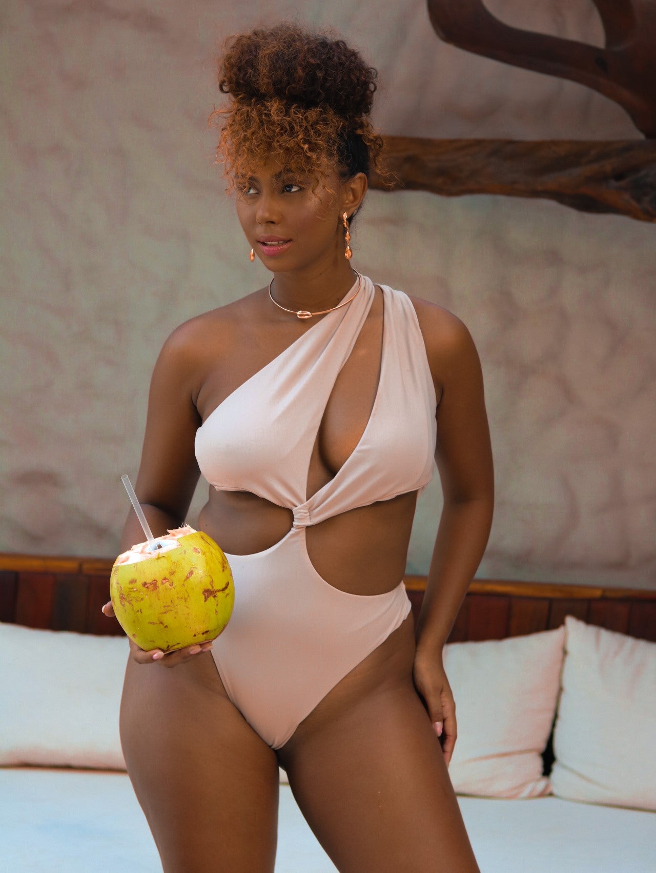 Modelo com um côco na mão vestindo maiô feminino assimétrico na cor nude..