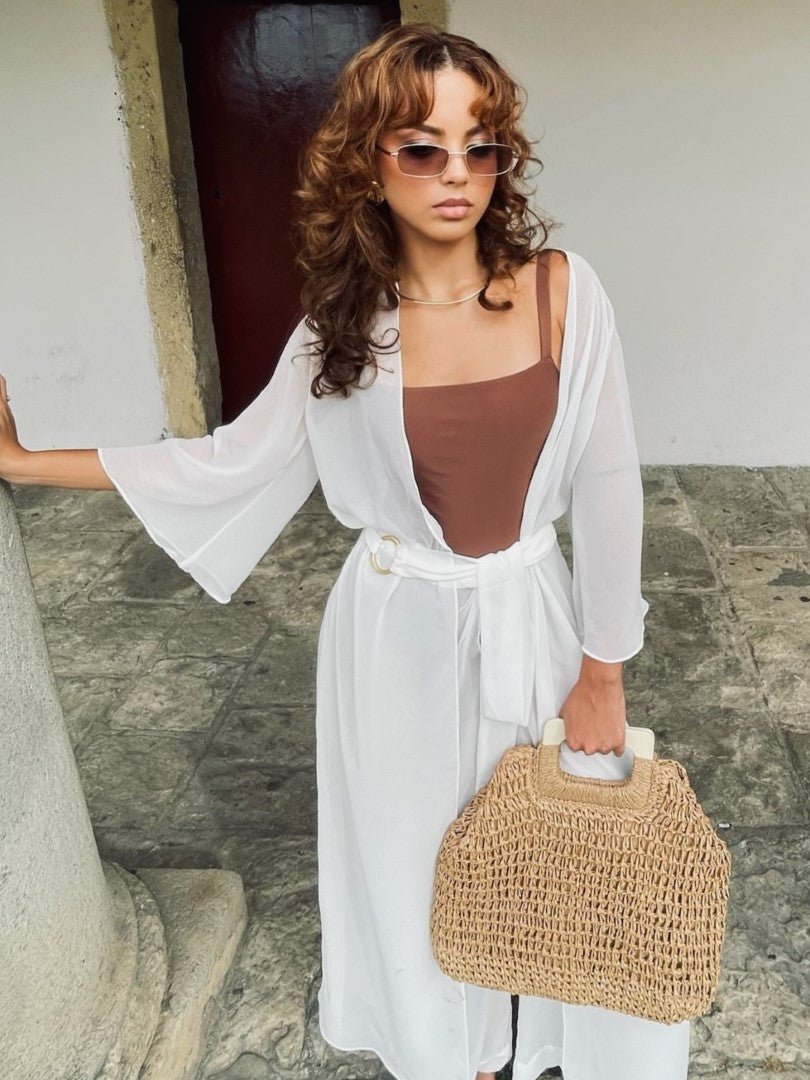 Modelo segurando bolsa de praia, vestindo maiô marrom e saida de praia elegante do tipo kimono longo branco transparente