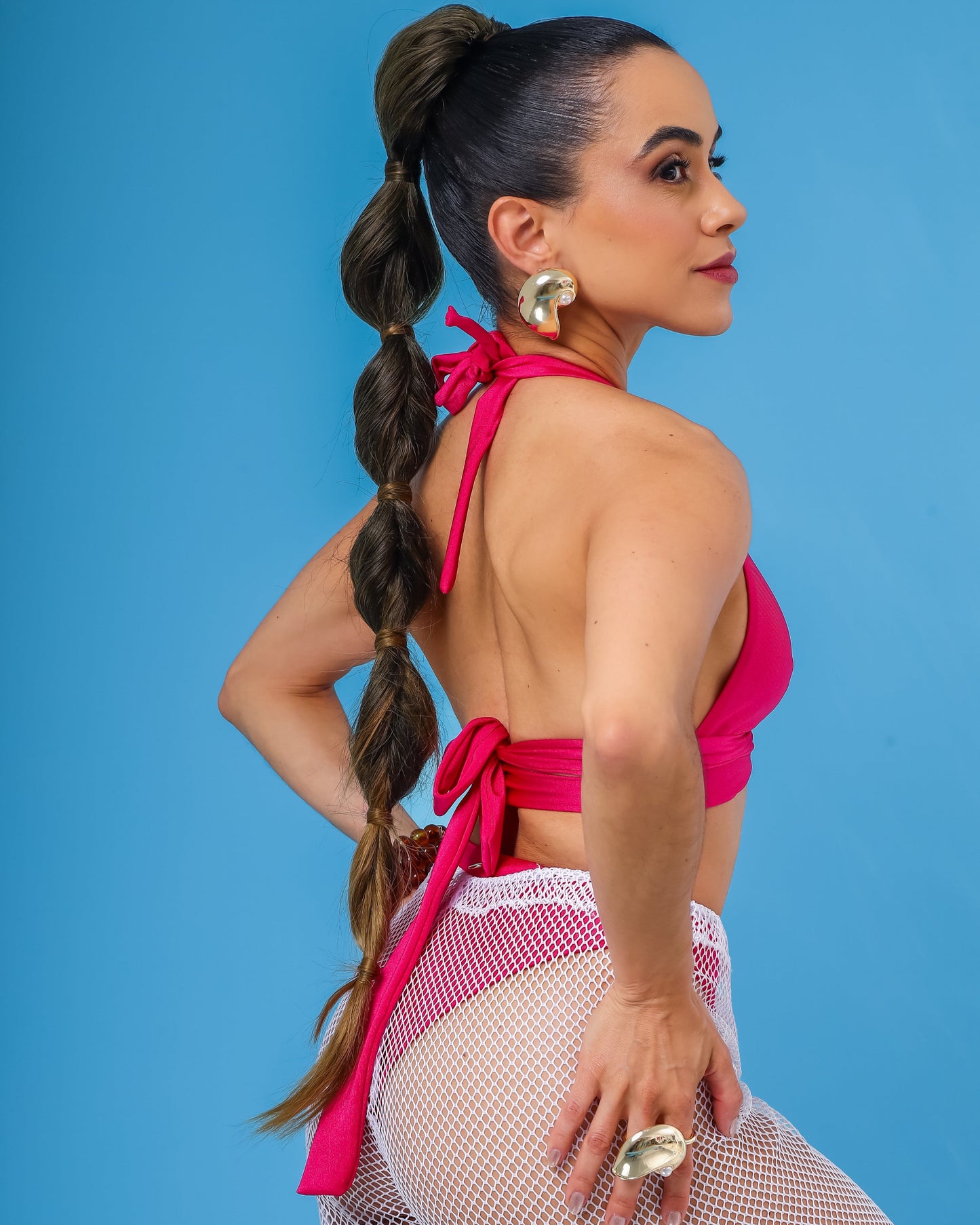 Close em modelo de lado vestindo top biquini rosa e calça de tela branca