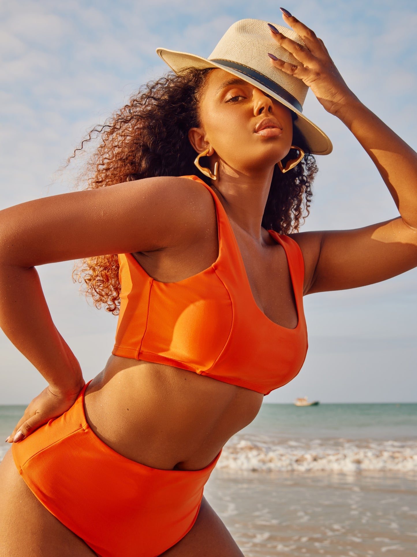 Modelo na beira-mar de Cabedelo vestindo um top biquini laranja com decote reto e uma calcinha biquini cintura alta laranja.