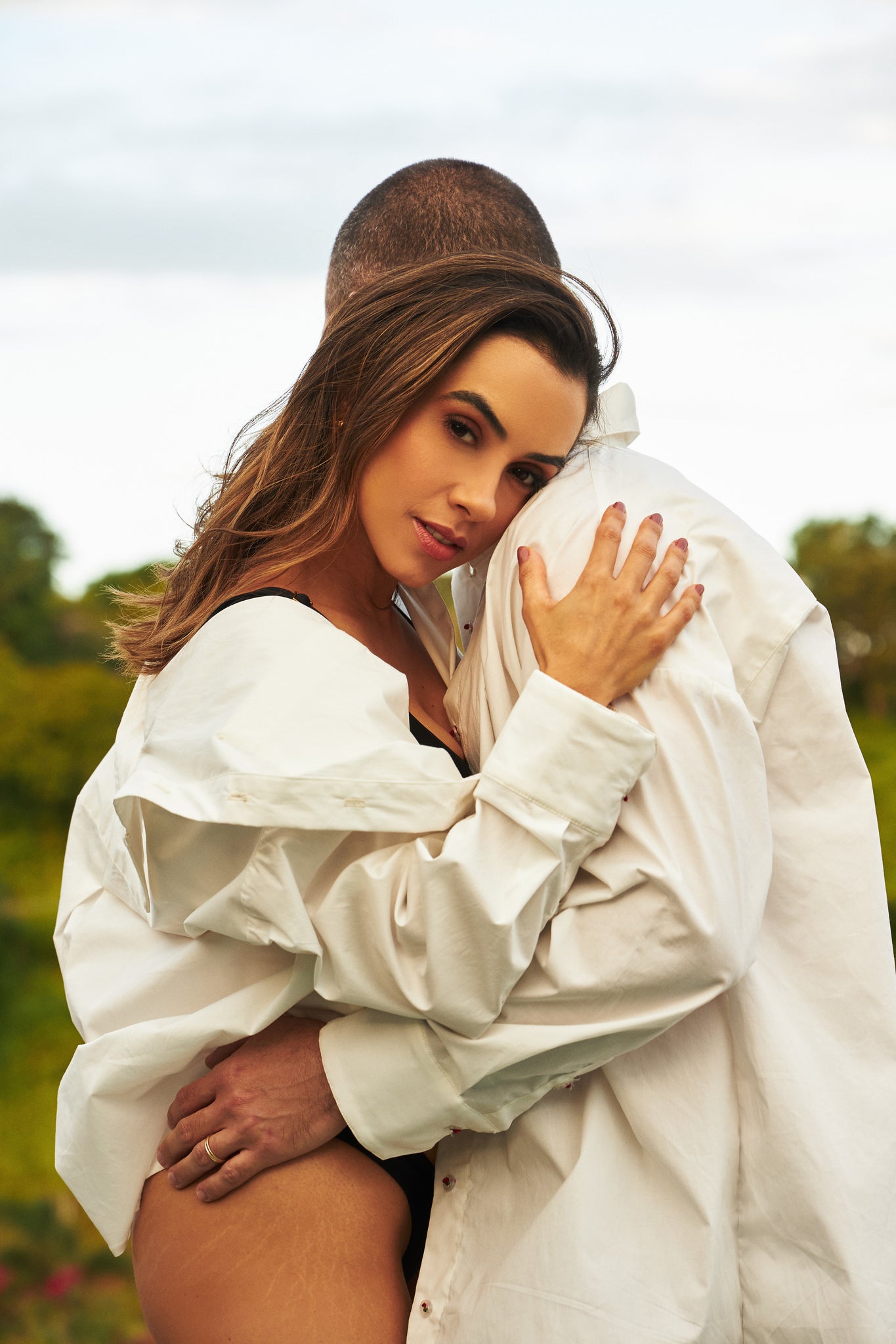 Casal abraçado vestindo camisa oversized branca unissex de manga longa.